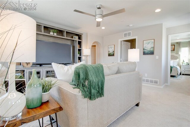 carpeted living room with built in shelves and ceiling fan