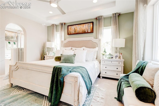 bedroom featuring light carpet, ceiling fan, and a tray ceiling