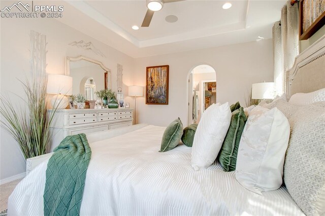 carpeted bedroom featuring ceiling fan and a tray ceiling