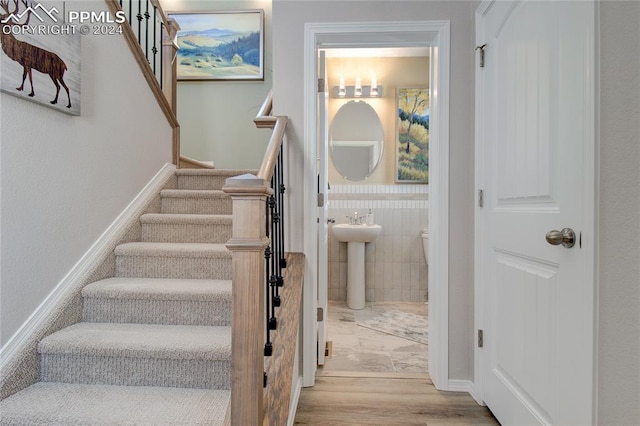 staircase with wood finished floors and tile walls