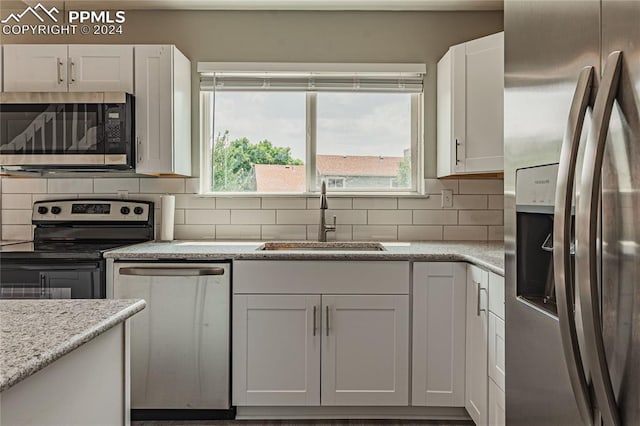 kitchen with stainless steel appliances, sink, decorative backsplash, light stone countertops, and white cabinetry