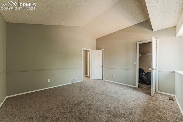 unfurnished bedroom with a textured ceiling, a closet, lofted ceiling, and carpet flooring