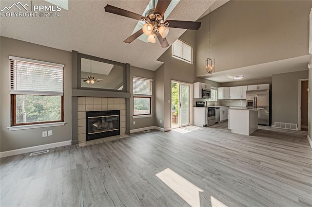 unfurnished living room with ceiling fan, a high ceiling, light hardwood / wood-style floors, a textured ceiling, and a tiled fireplace