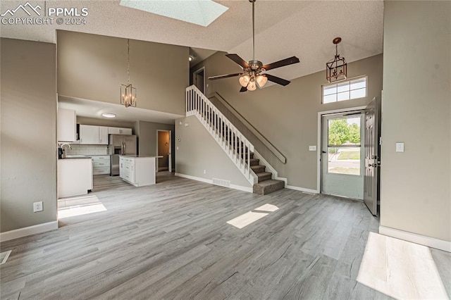 foyer entrance with high vaulted ceiling, a skylight, ceiling fan with notable chandelier, and light hardwood / wood-style floors