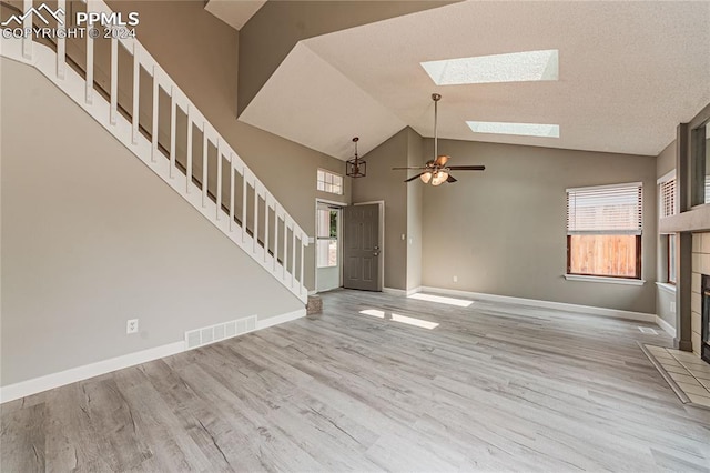 foyer featuring ceiling fan, high vaulted ceiling, a skylight, light hardwood / wood-style flooring, and a tiled fireplace