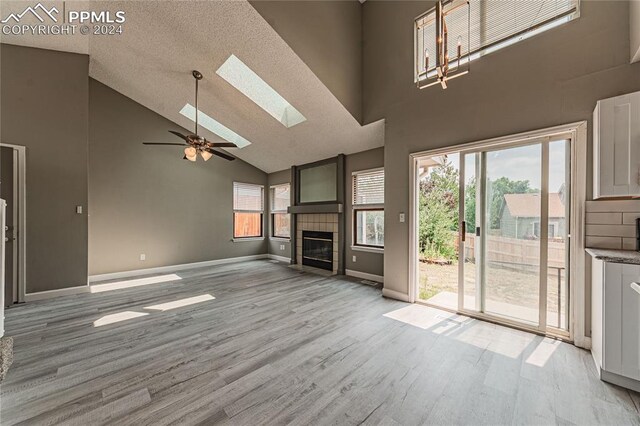 unfurnished living room with a healthy amount of sunlight, high vaulted ceiling, a skylight, light hardwood / wood-style floors, and a tile fireplace