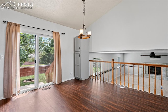 unfurnished room with ceiling fan with notable chandelier, vaulted ceiling, dark hardwood / wood-style flooring, and a textured ceiling