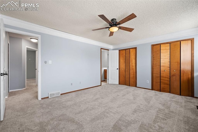 unfurnished bedroom featuring ceiling fan, a textured ceiling, two closets, and light carpet