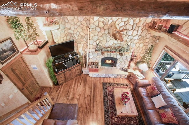 living room featuring beam ceiling, a stone fireplace, and hardwood / wood-style floors