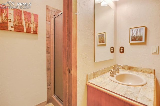 bathroom featuring a shower with shower door and vanity