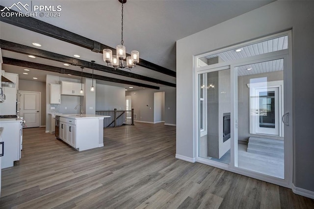 kitchen featuring hanging light fixtures, a notable chandelier, beamed ceiling, a kitchen island with sink, and white cabinets