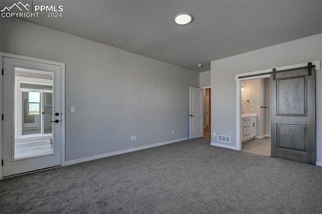 unfurnished bedroom with ensuite bathroom, a barn door, and light colored carpet