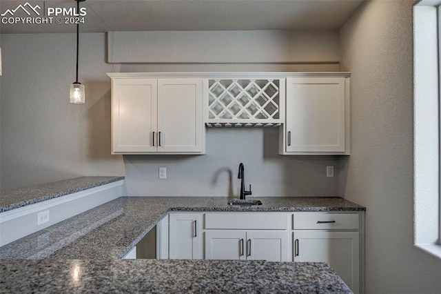 kitchen featuring white cabinetry, dark stone counters, sink, and hanging light fixtures