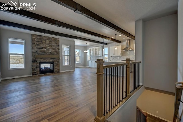 living room with wood-type flooring, beam ceiling, a stone fireplace, and a wealth of natural light