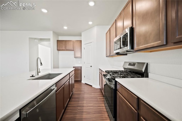 kitchen featuring stainless steel appliances, light countertops, a sink, and dark wood-type flooring