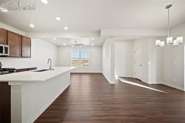 kitchen featuring a sink, light countertops, stainless steel microwave, dark wood finished floors, and an island with sink