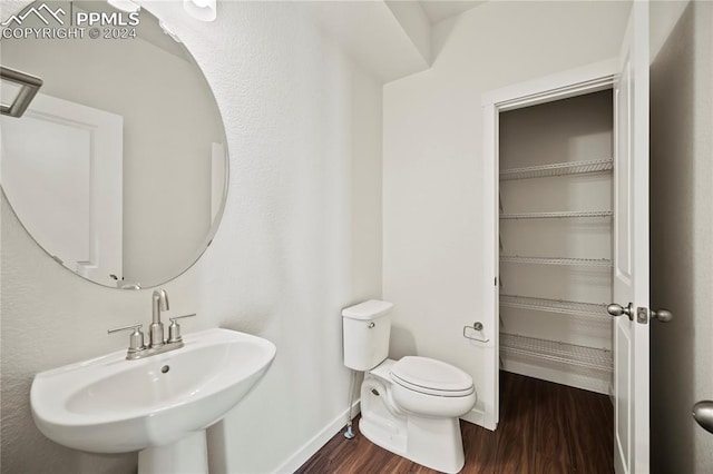 half bathroom with toilet, a sink, baseboards, and wood finished floors