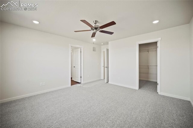 unfurnished bedroom with ceiling fan, a spacious closet, light carpet, and a closet