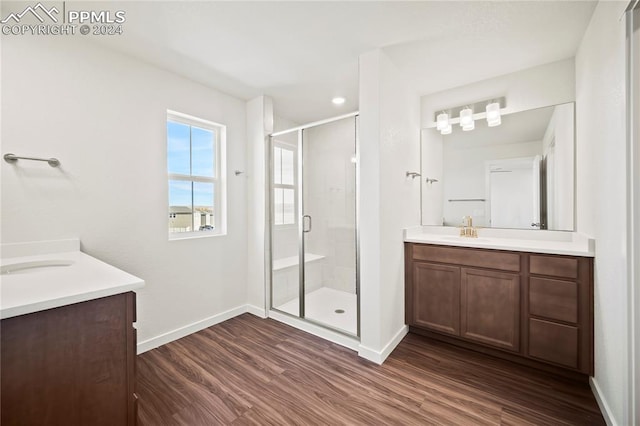 bathroom featuring two vanities, a sink, a shower stall, wood finished floors, and baseboards