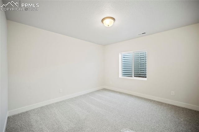 carpeted empty room with visible vents, a textured ceiling, and baseboards