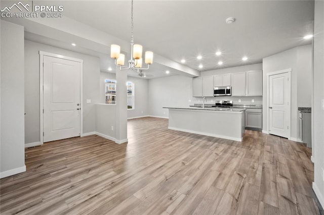 kitchen with decorative light fixtures, an island with sink, a notable chandelier, light hardwood / wood-style floors, and stainless steel appliances