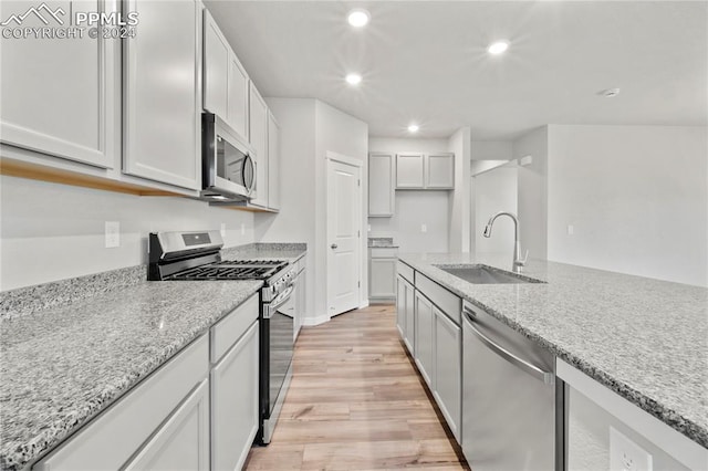 kitchen with white cabinets, sink, light hardwood / wood-style flooring, appliances with stainless steel finishes, and light stone counters