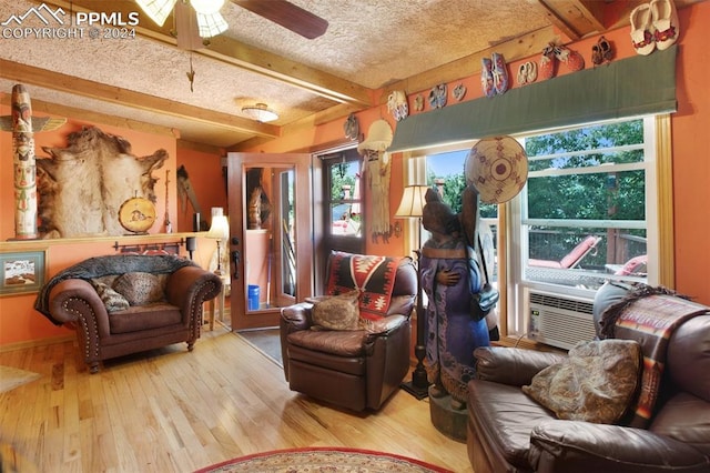 living room featuring hardwood / wood-style flooring, ceiling fan, cooling unit, beam ceiling, and a textured ceiling