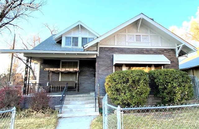 craftsman-style house with covered porch, a fenced front yard, and brick siding