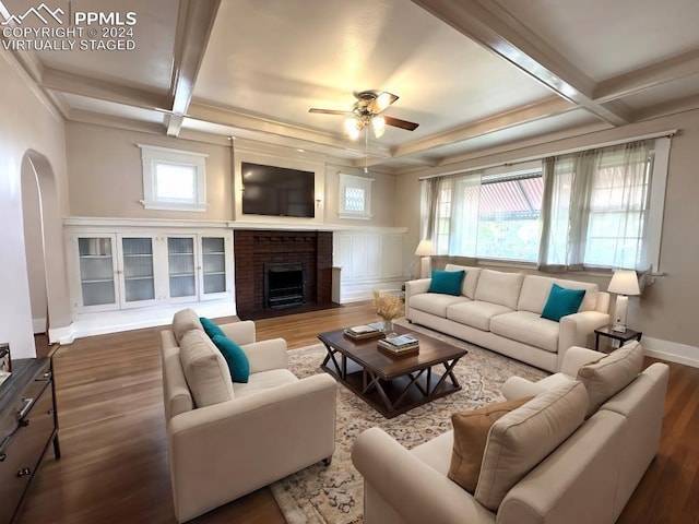 living room featuring arched walkways, a brick fireplace, coffered ceiling, and dark wood finished floors