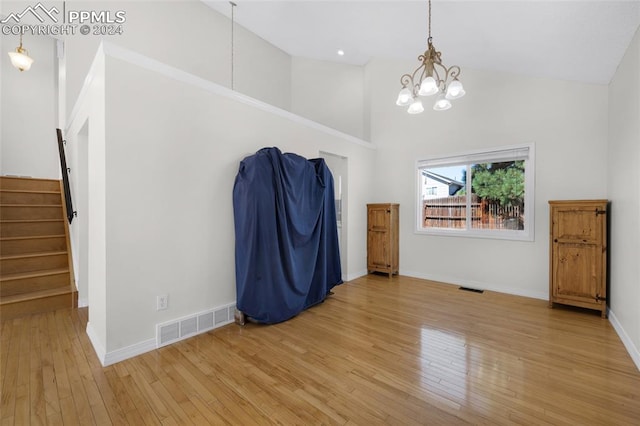 spare room with high vaulted ceiling, a notable chandelier, and light hardwood / wood-style floors