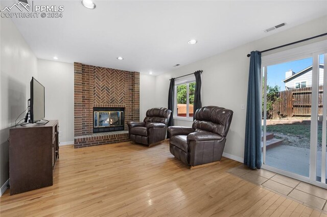 living room with light hardwood / wood-style floors, brick wall, and a brick fireplace