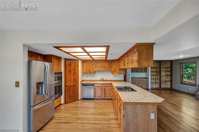 kitchen with sink, tile countertops, stainless steel appliances, and light hardwood / wood-style floors