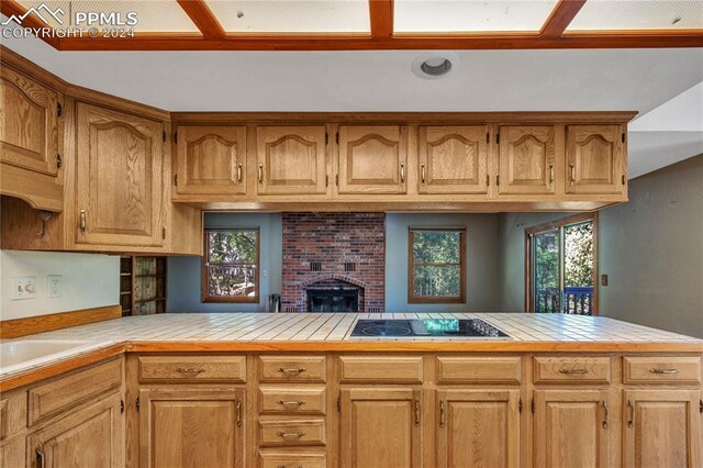 kitchen featuring black electric cooktop, a wealth of natural light, kitchen peninsula, and a brick fireplace