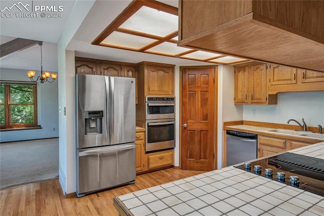 kitchen with light hardwood / wood-style flooring, appliances with stainless steel finishes, a notable chandelier, sink, and tile countertops