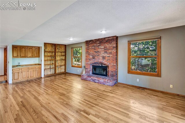 unfurnished living room with a fireplace, a textured ceiling, light hardwood / wood-style floors, and brick wall