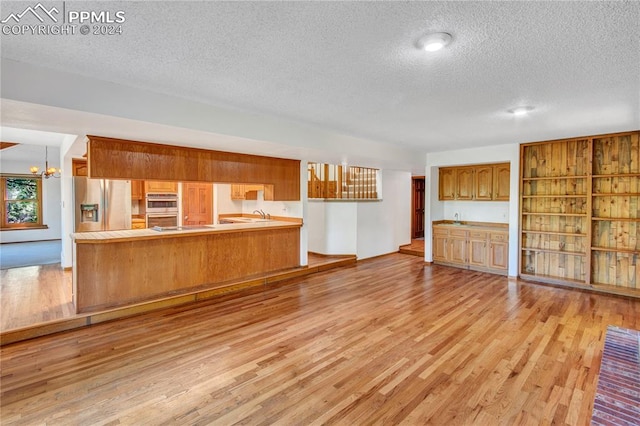 unfurnished living room featuring an inviting chandelier, a textured ceiling, and light hardwood / wood-style floors