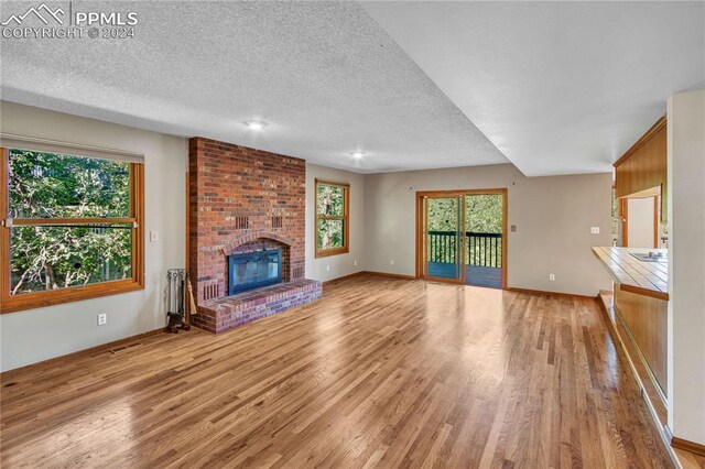 unfurnished living room with a fireplace, a textured ceiling, brick wall, and light hardwood / wood-style floors