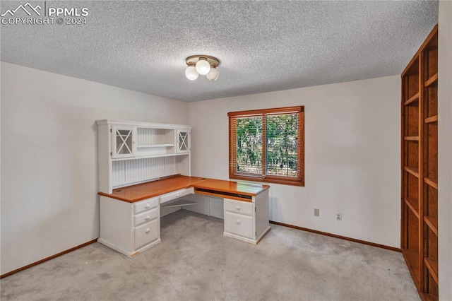 unfurnished office with light colored carpet, built in desk, and a textured ceiling