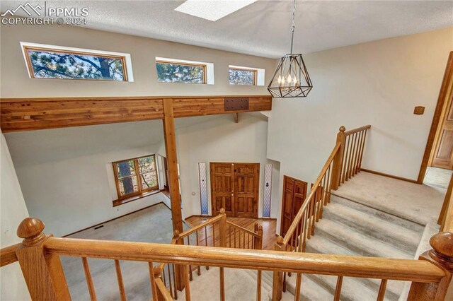 stairway with a textured ceiling, a skylight, a chandelier, and light carpet