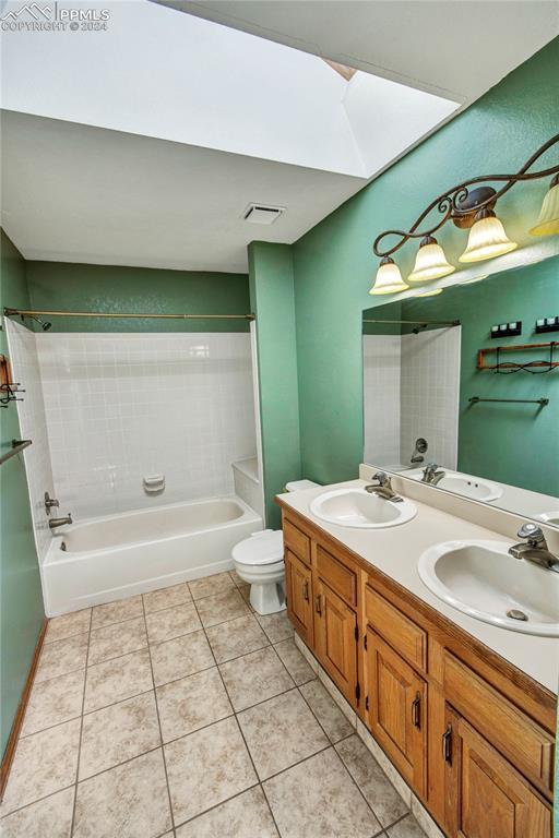 full bathroom with tiled shower / bath, double sink vanity, toilet, and tile patterned flooring