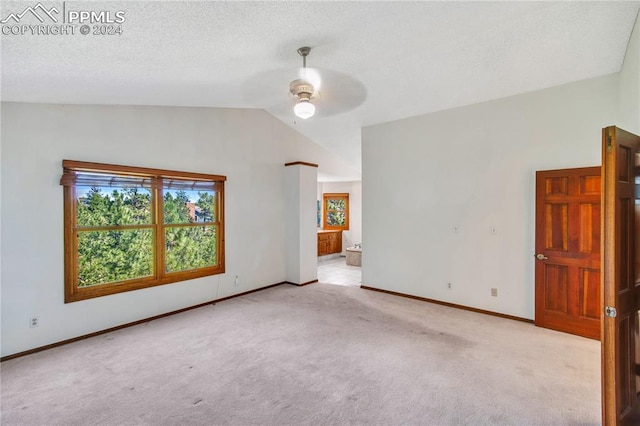 spare room featuring lofted ceiling, a textured ceiling, light colored carpet, and ceiling fan