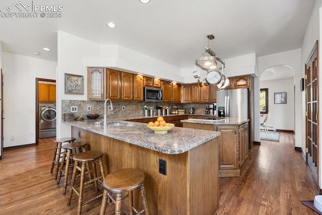 kitchen with a breakfast bar, washer / dryer, appliances with stainless steel finishes, kitchen peninsula, and decorative backsplash