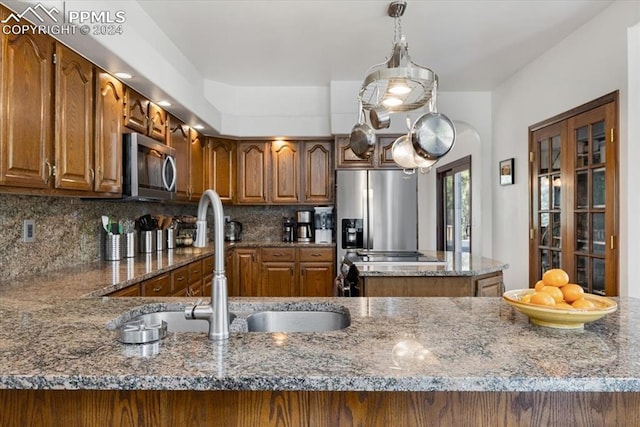 kitchen featuring stainless steel appliances, hanging light fixtures, decorative backsplash, and dark stone countertops