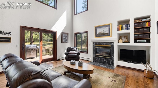 living room with built in features, a high ceiling, a fireplace, wood-type flooring, and a baseboard radiator