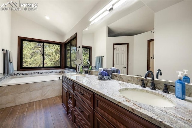 bathroom with lofted ceiling, vanity, and tiled tub