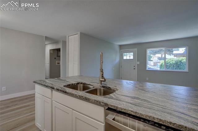 kitchen with sink, light hardwood / wood-style flooring, light stone countertops, white cabinets, and stainless steel dishwasher