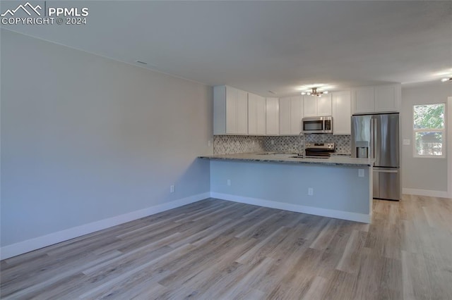 kitchen with appliances with stainless steel finishes, backsplash, white cabinets, kitchen peninsula, and light wood-type flooring