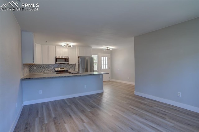 kitchen with white cabinets, backsplash, kitchen peninsula, stainless steel appliances, and light wood-type flooring