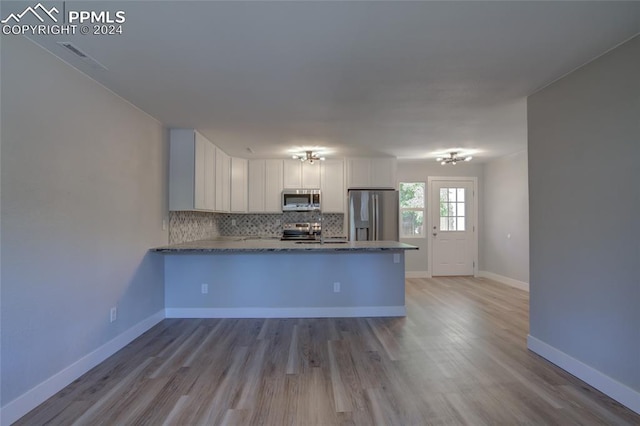 kitchen featuring tasteful backsplash, kitchen peninsula, stainless steel appliances, light hardwood / wood-style floors, and white cabinets