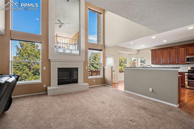 carpeted living room featuring a textured ceiling, ceiling fan, a high ceiling, and a brick fireplace